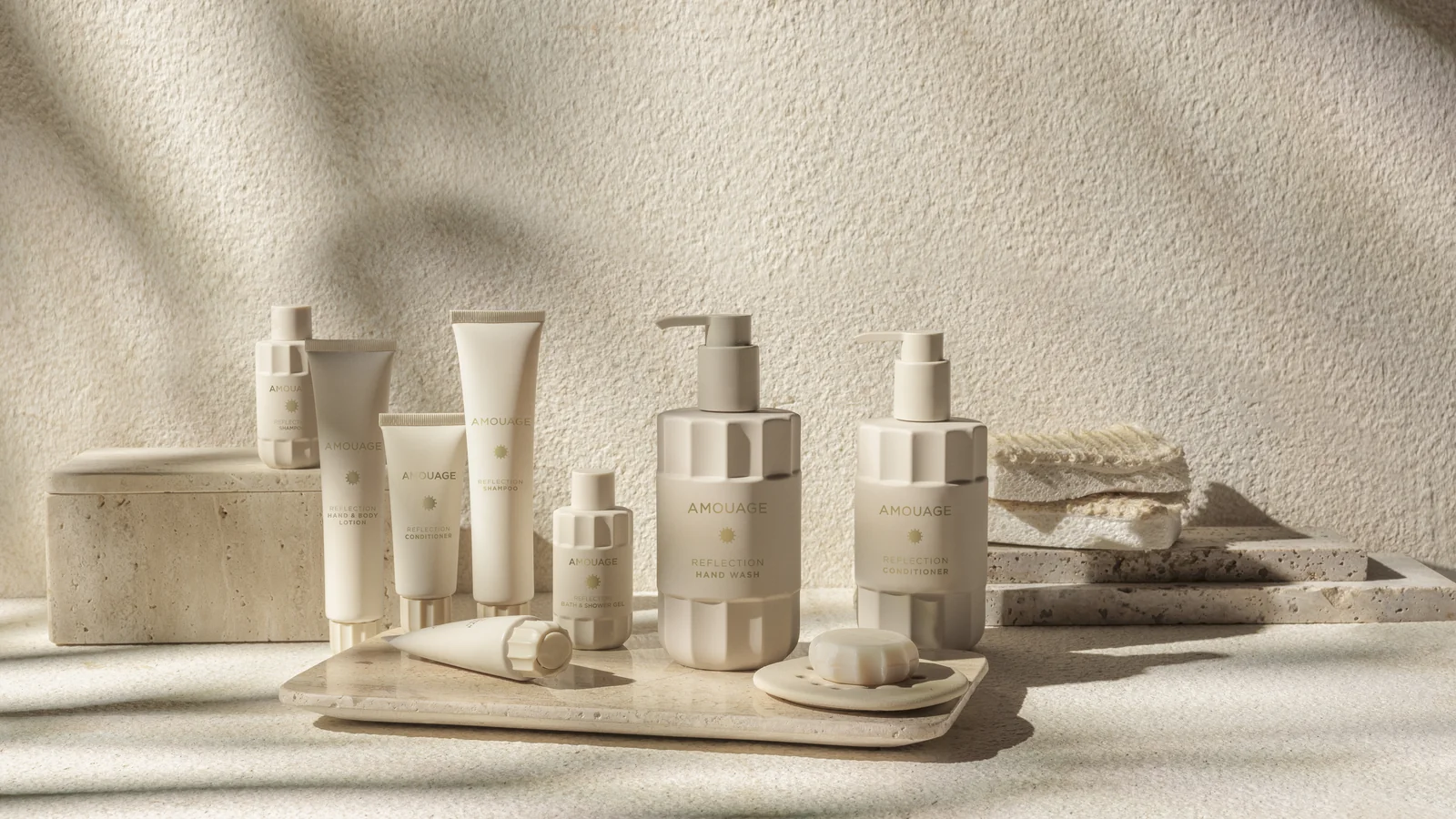 The Amouage Reflection line, cream bottles and tubes, on a stone counter in morning light