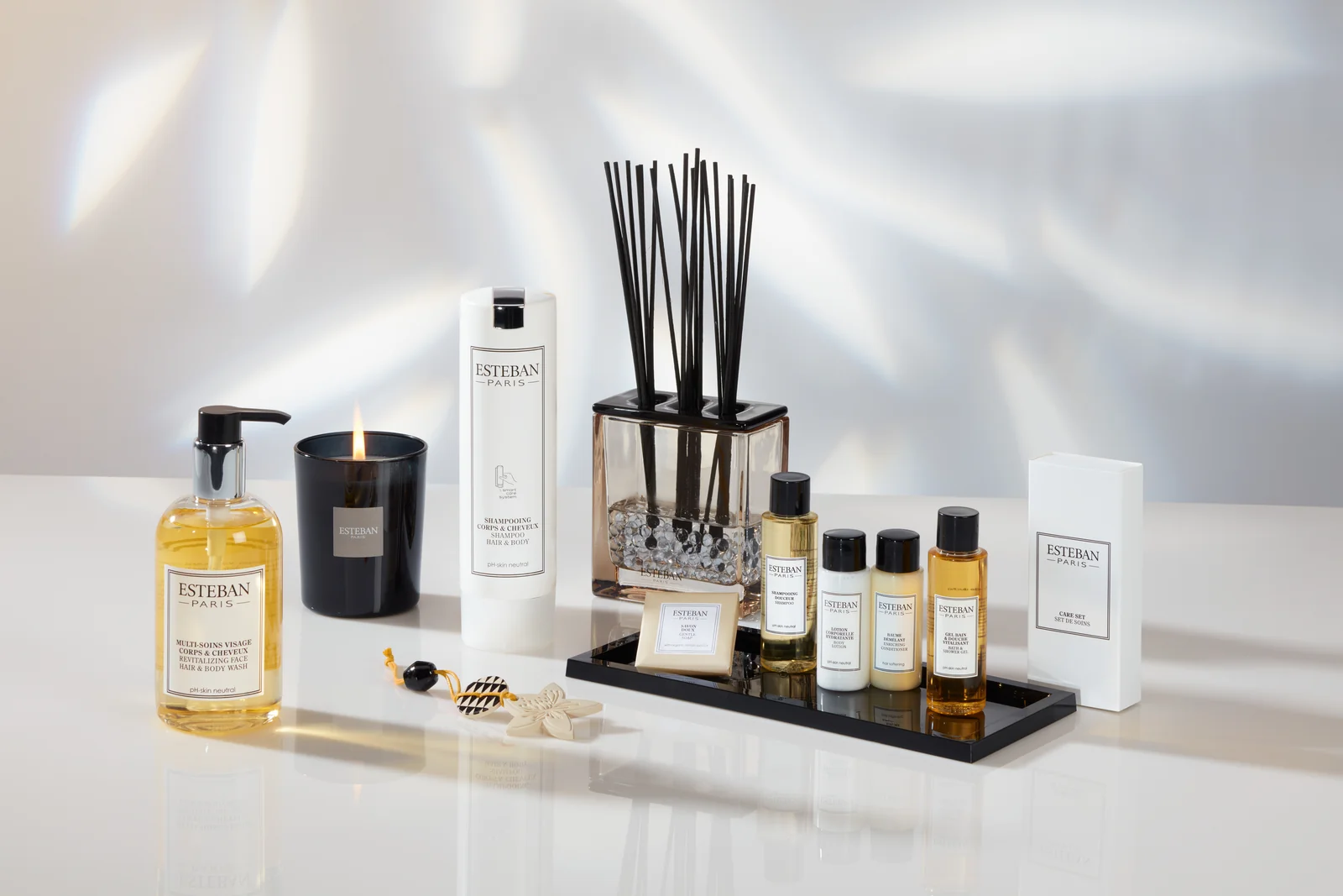 Produse Esteban, săpun lichid, lumânare și difuzor, pe o tavă neagră în lumină naturală