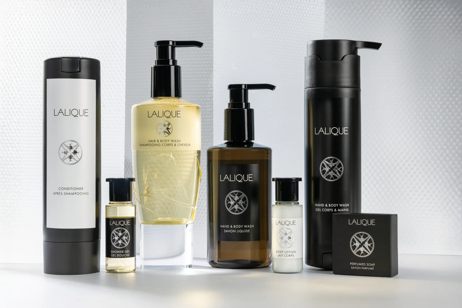 The Lalique line — large bottles, pump bottles and miniatures — on a textured white background